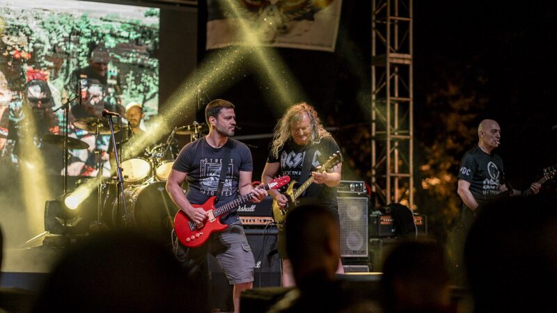 1280px Live rock concert featuring musicians playing electric guitars on stage at night with vibrant lights and an enthusiastic crowd present