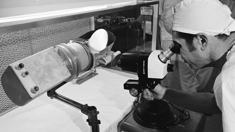 1280px View of scientist looking at a Surveyor III components with a microscope in a Lunar Receiving Laboratory sterile vacuum cabinet %28s70 22401%29